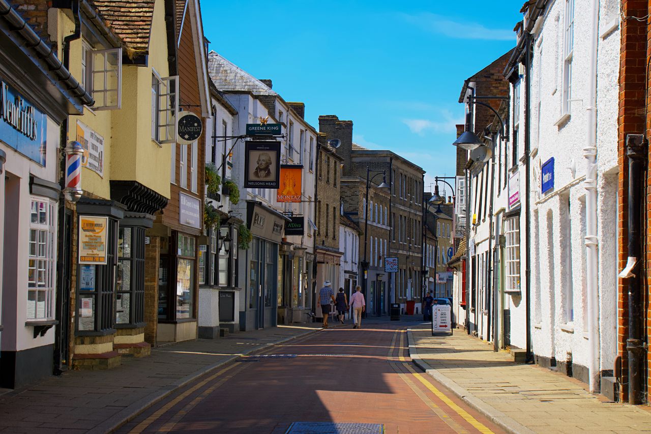 A picturesque street in Cambridge, England, lined with shops and people strolling on a sunny day.